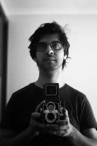 A photo of myself. The photo is in black and white, and i am taking a photo of myself, using a twin lens camera at my waist, looking towards a mirror. My hair is a bit scruffy.
